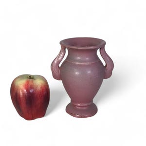 Może przedstawiać: Mały, różowy ceramiczny wazon z dwoma uchwytami. Wazon ma klasyczny, grecki design i idealnie nadaje się do wyeksponowania pojedynczego kwiatu lub małego bukietu.