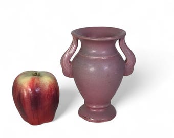 Może przedstawiać: Mały, różowy ceramiczny wazon z dwoma uchwytami. Wazon ma klasyczny, grecki design i idealnie nadaje się do wyeksponowania pojedynczego kwiatu lub małego bukietu.