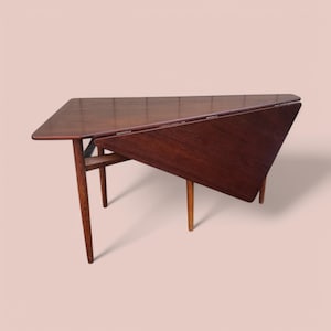 May include: A dark wood triangular folding table with a geometric design. The table has four legs and is made of solid wood.