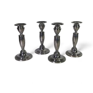 Può includere: Set di quattro candelieri d'argento. Ogni candelabro ha una base rotonda e uno stelo alto e sottile con una coppa nella parte superiore.
