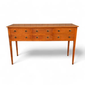 May include: A wooden dresser with a light brown finish. It has seven drawers with dark knobs and four slender legs. The dresser is rectangular and has a polished surface.