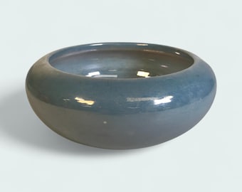 May include: A round, ceramic bowl with a wide rim and a glossy finish. The bowl has a gradient color scheme, transitioning from a darker blue at the base to a lighter blue at the rim. The interior reflects light.