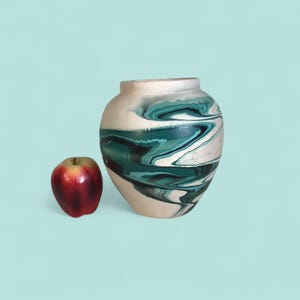 May include: A ceramic vase with a cream-colored base and teal and black swirled design. A red apple sits to the left of the vase. The vase has a rounded shape and a wide opening.