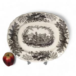 May include: A white oval platter with a black and white landscape scene in the centre. The border of the platter is decorated with a black and white floral pattern.