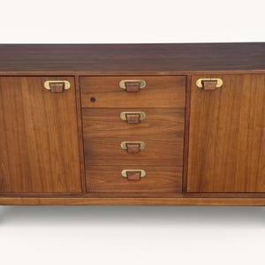 May include: A mid-century modern wooden cabinet with a dark brown finish. It features two doors with brass handles on the sides and four drawers in the center. The cabinet is supported by four legs.
