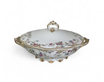 May include: A white porcelain serving dish with a lid, featuring a floral pattern in shades of pink, blue, and gold. The dish has a scalloped edge and a decorative handle.
