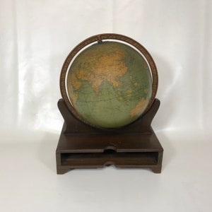 May include: A vintage wooden globe stand with a green globe featuring a detailed map of the world. The globe is mounted on a wooden base with a drawer.