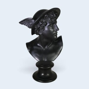 May include: A matte black bust of a figure wearing a winged petasos hat. The sculpture features detailed facial features, curly hair, and a smooth neck and shoulder area, all resting on a circular pedestal base with a polished, dark finish.
