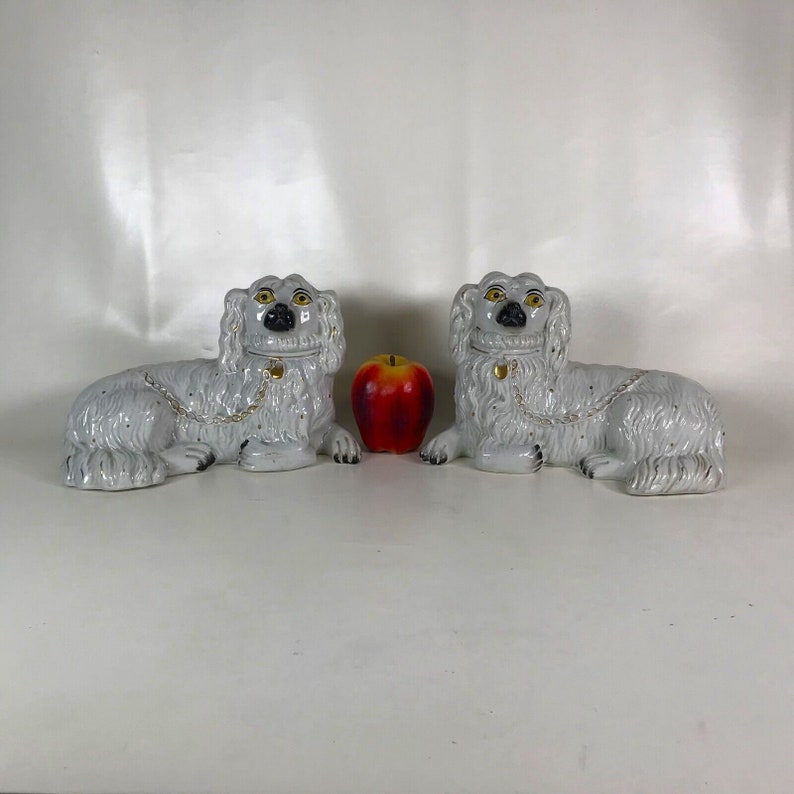 May include: Pair of white porcelain dog figurines with black eyes and gold accents. The dogs are lying down with their heads turned to the side.