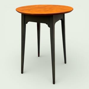 May include: A small, round side table with a dark green base and a warm, orange-brown tabletop. The table has four slender legs and a simple, elegant design, perfect for a living room or entryway. The tabletop is approximately 24 inches in diameter.