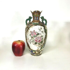 May include: A white porcelain vase with a floral design and gold accents. The vase has two handles and a decorative top. The vase is decorated with pink, red, and green flowers.
