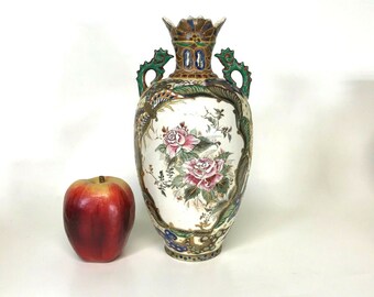 May include: A white porcelain vase with a floral design and gold accents. The vase has two handles and a decorative top. The vase is decorated with pink, red, and green flowers.