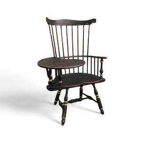May include: A black wooden armchair with a small round table attached to the right arm. The chair has a high back and a curved top. The table is painted black with gold accents. The chair is a traditional style.