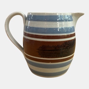May include: A ceramic jug with a curved handle and spout. The jug features horizontal stripes in blue, brown, and white, with a fern-like design. The jug is a vintage style and is suitable for serving beverages.