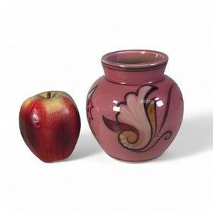 May include: A small pink ceramic vase with a floral design. The vase has a rounded body and a narrow opening. The floral design is in shades of pink, orange, and black.