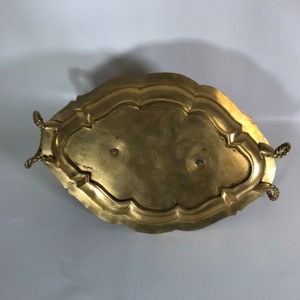 May include: A gold-toned metal serving tray with a rope-like handle on each side. The tray has a scalloped edge and a raised center.