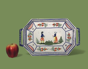 May include: A rectangular, white ceramic serving tray with blue handles and a decorative border. The tray features a hand-painted scene of two figures in traditional clothing, surrounded by floral and leaf motifs. A red apple sits to the left.