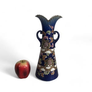May include: A tall, blue and gold ceramic vase with a floral design. The vase has two handles and a wide mouth.