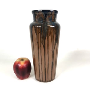 Pode incluir: Um vaso de cerâmica marrom com um esmalte azul escuro e um esmalte marrom com gotejamento. O vaso é alto e fino com uma base arredondada.