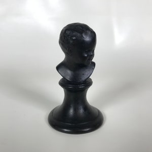 May include: A black ceramic bust of a child's head on a black pedestal.