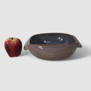 May include: A square brown ceramic baking dish with two handles. The dish has a light blue glaze on the inside.