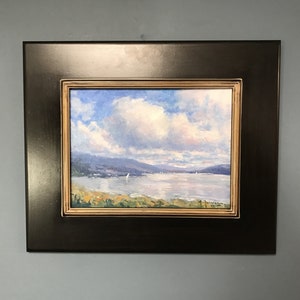 Peut inclure: Une peinture encadrée représentant un paysage marin avec un ciel bleu, des nuages blancs et une étendue d'eau avec des voiliers au loin. La peinture est encadrée dans un cadre noir avec une bordure intérieure dorée.