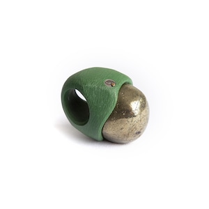 May include: A ring featuring a textured, matte green band with a visible wood grain pattern. A large, spherical, metallic pyrite stone with a reflective, brassy gold surface is set into the side of the band, secured by a small, circular metal rivet.