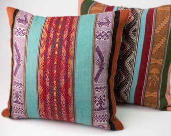 May include: Two decorative throw pillows with a colorful striped pattern featuring geometric designs and traditional Peruvian motifs. The pillows are made of woven fabric and have a soft, textured feel.