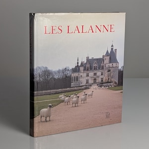 Op de afbeelding: Een boek getiteld "LES LALANNE" met een foto van een kasteel en schapen op de omslag. De titel is rood. De afbeelding heeft een vintage uitstraling, wat wijst op een historisch of kunstgerelateerd thema.