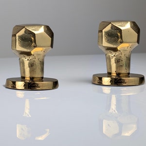 May include: Two gold-toned, faceted, round door knobs with a hammered finish. The knobs are mounted on a round base.