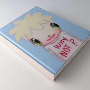 Puede incluir: Un libro azul claro con una ilustración de dibujos animados de una persona con cabello rubio que lleva una camisa blanca con las palabras "WHY NOT?" impresas en rojo.