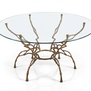 Könnte beinhalten: Ein runder Couchtisch mit Glasplatte und einem Metallgestell in Bronzefarbe. Das Gestell hat ein kompliziertes, organisches Design mit mehreren gebogenen Beinen und Stützen, wodurch ein optisch auffälliges Möbelstück entsteht.