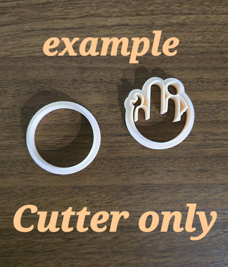Op de afbeelding: Twee witte plastic koekjesvormpjes. De ene is een eenvoudige ronde ring, de andere is een ronde uitsteker met een intern ontwerp van een gestileerd figuur met een opgeheven hand. De tekst "example" en "Cutter only" zijn in de afbeelding zichtbaar.