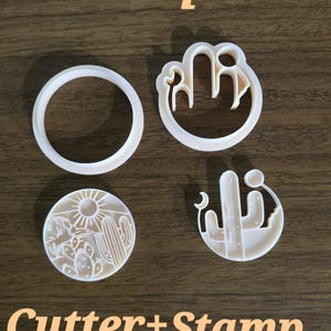 Op de afbeelding: Een set witte plastic kleisnijders en stempels. E&eacute;n ronde snijder, &eacute;&eacute;n ronde stempel met een woestijnlandschap met zon en cactussen, en twee ronde stempels met woestijn-thema contouren inclusief cactussen en een maansikkel.