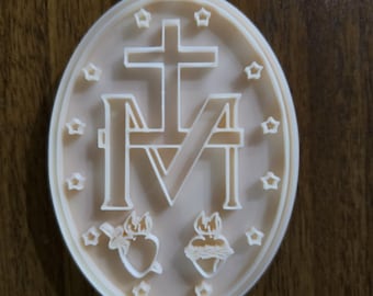 Op de afbeelding: Een ovaalvormige beige plaquette met een reliëfontwerp van het symbool van de Wonderdadige Medaille. Het midden toont een grote letter M met een kruis erboven, geflankeerd door twee harten onderaan, omringd door twaalf kleine vijfpuntige sterren.