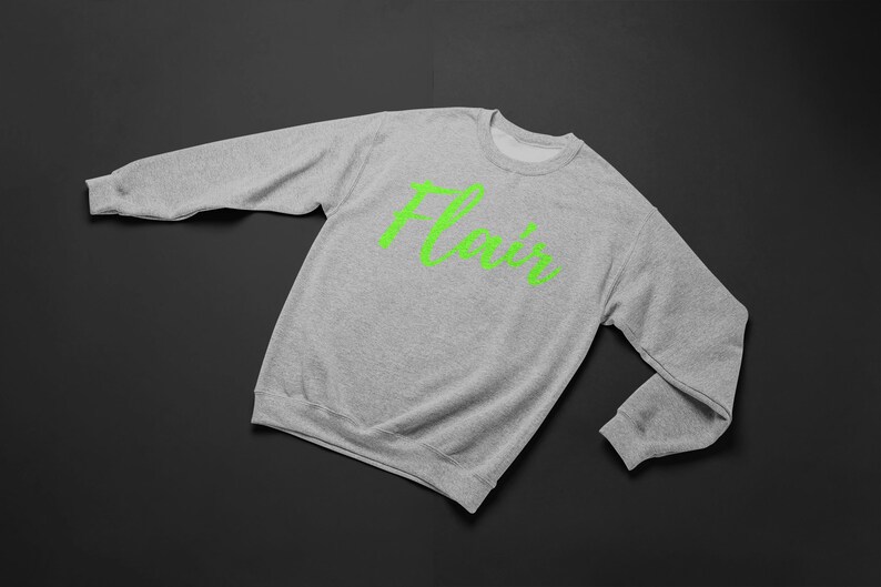 K&ouml;nnte beinhalten: Ein grauer Pullover mit dem Wort "Flair" in Gr&uuml;n auf der Vorderseite.