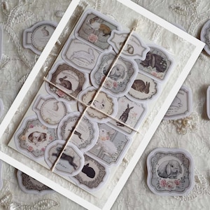 May include: A sheet of vintage-style bunny rabbit stickers with a variety of designs. The stickers are printed on white paper with a light brown background and feature illustrations of rabbits in various poses. The stickers are perfect for adding a touch of whimsy to your crafts, journals, or planners.