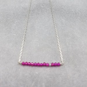 May include: A silver chain necklace with a row of pink and purple beads.