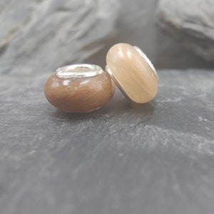 May include: Two round beads with a light brown, textured surface and silver-colored metal accents. One bead is a darker brown color. The beads are likely for jewelry making or crafting.