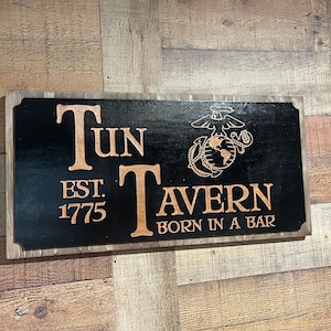 May include: Wooden sign with the words "Tun Tavern" and "Born in a Bar" in a light brown color, set against a black background. The sign also features the Marine Corps emblem and the year "EST. 1775".