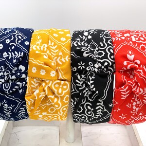 May include: Four fabric headbands with a knotted design. The headbands are in blue, yellow, black, and red with a white paisley pattern.