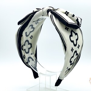 May include: A white headband with a black and white geometric pattern. The headband is tied in a bow at the top.