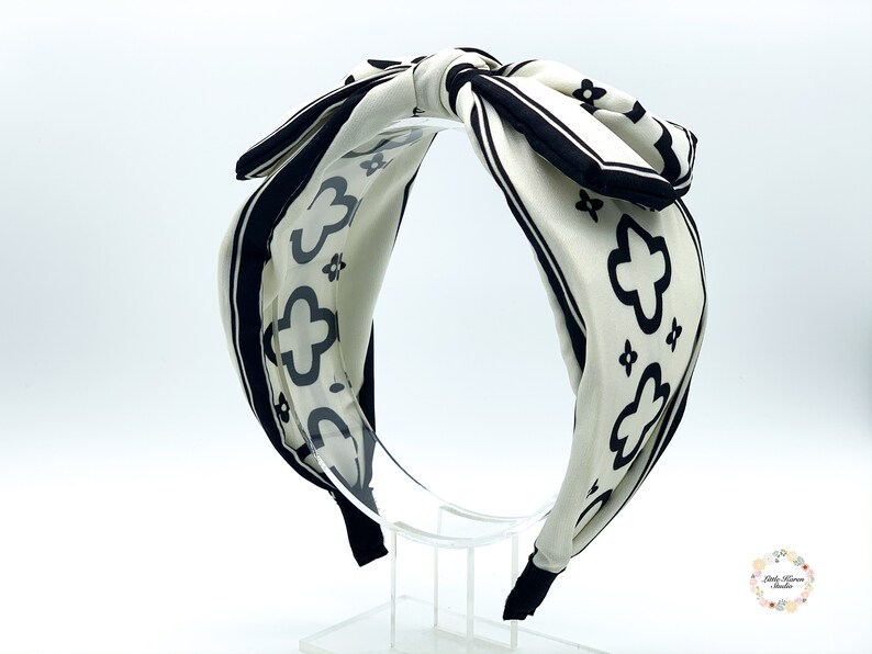 May include: A white headband with a black and white geometric pattern. The headband is tied in a bow at the top.
