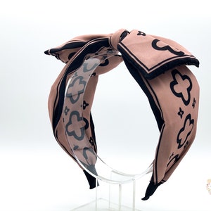 May include: A pink and black patterned headband with a large bow. The headband is made of fabric and has a black elastic band.