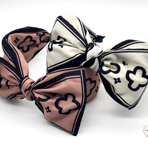May include: Two fabric headbands with large bows. One headband is pink with black and white floral print, the other is white with black and white floral print.