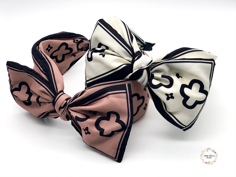 May include: Two fabric headbands with large bows. One headband is pink with black and white floral print, the other is white with black and white floral print.