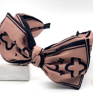 May include: A brown headband with a large black and white patterned bow. The bow is tied in a knot and the headband is made of a soft, stretchy material.