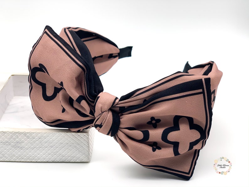 May include: A brown headband with a large black and white patterned bow. The bow is tied in a knot and the headband is made of a soft, stretchy material.