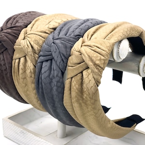 May include: Three knotted headbands in brown, beige, and gray. The headbands are made of a soft, textured fabric and have a wide, comfortable fit.