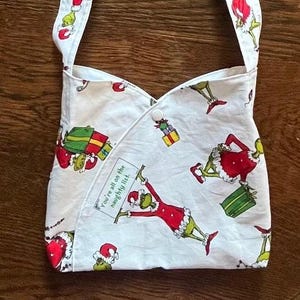 May include: White fabric tote bag with a green Grinch character print. The bag has a red and green strap and features the text "You're all on the naughty list."